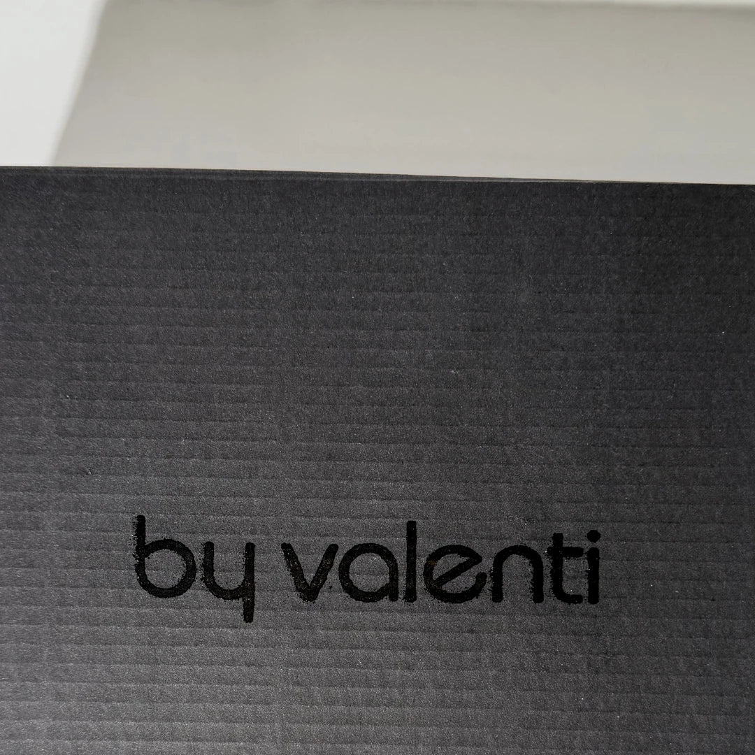 Text 'by valenti' on a textured black surface