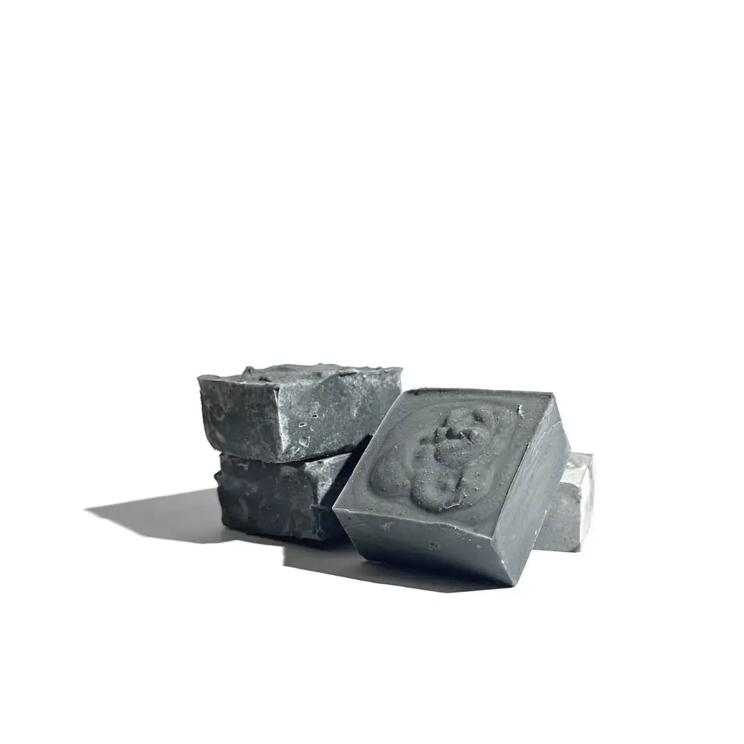 Four charcoal black bars of By Valenti Black Clay Facial Soap on a white background
