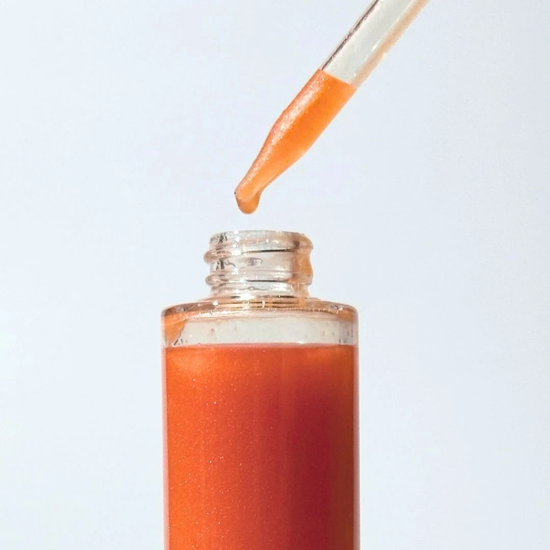 Bottle of orange-gold By Valenti Estate a Barcola shimmering body oil liquid with a dropper on a light gray background