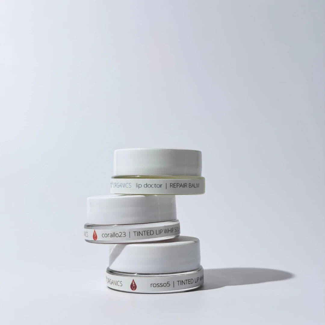 Stack of by valenti lip balm containers on a light gray background