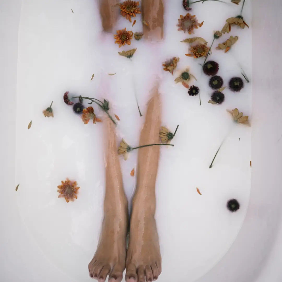 Person's legs in a bathtub filled with bubbles and flowers