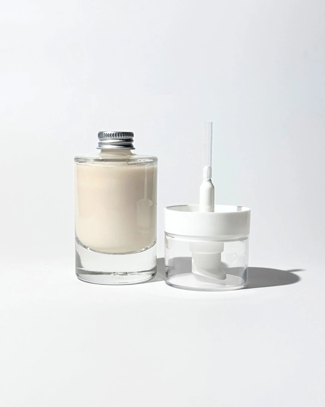 By Valenti glass refill bottle of face moisturizer and reusable pump on a light gray background