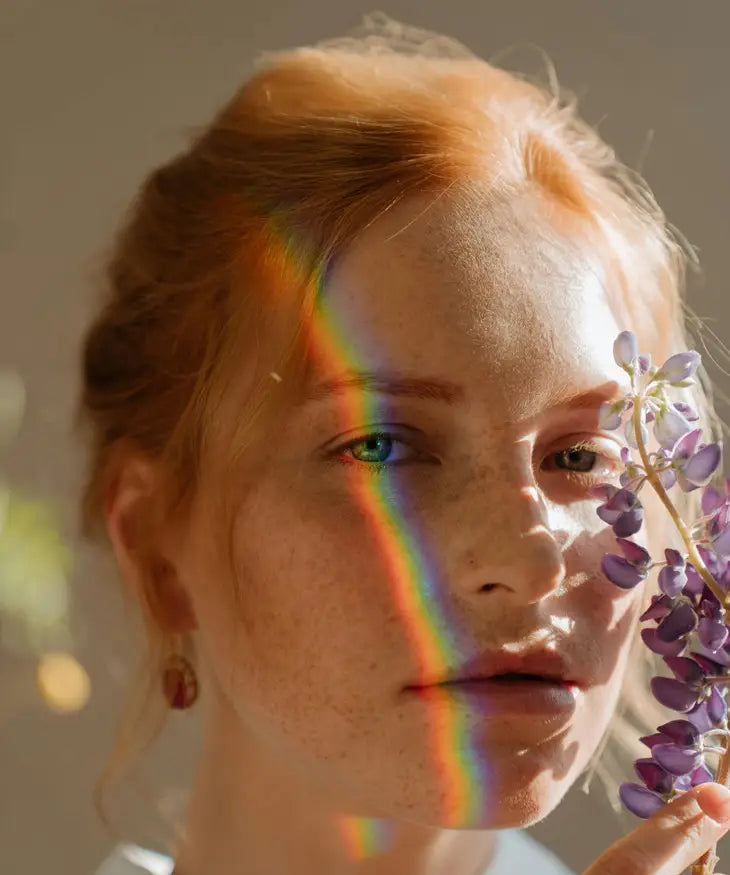Woman with a rainbow effect over their face holding purple flowers.